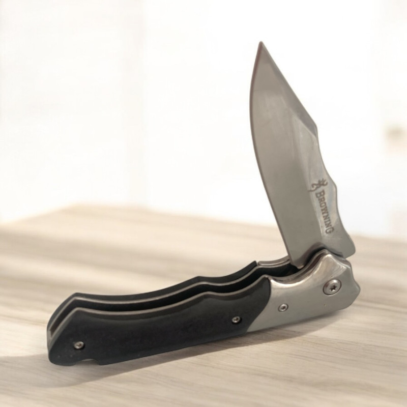 Нож Browning Silver Edge изправен върху дървена маса с отблясъци от светлина Сгъваем нож Browning със сребристо острие и черна дръжка върху светла повърхност