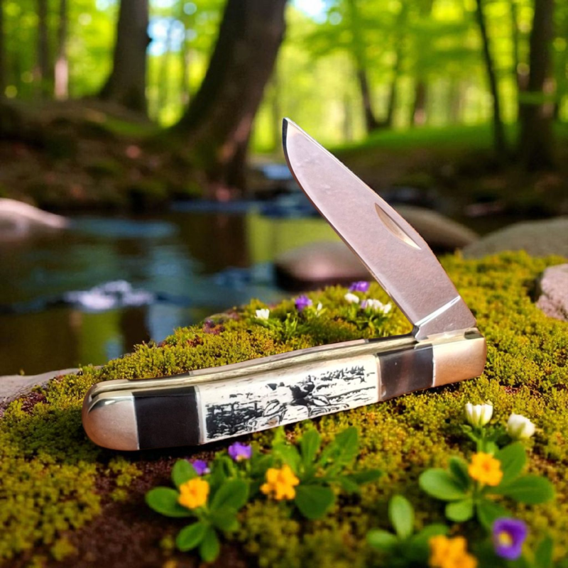 Нож с изображение на елен, разположен върху пън в зелена природа Сгъваем нож Forest Stag с гравирана дръжка, поставен върху дървена дъска и камъни