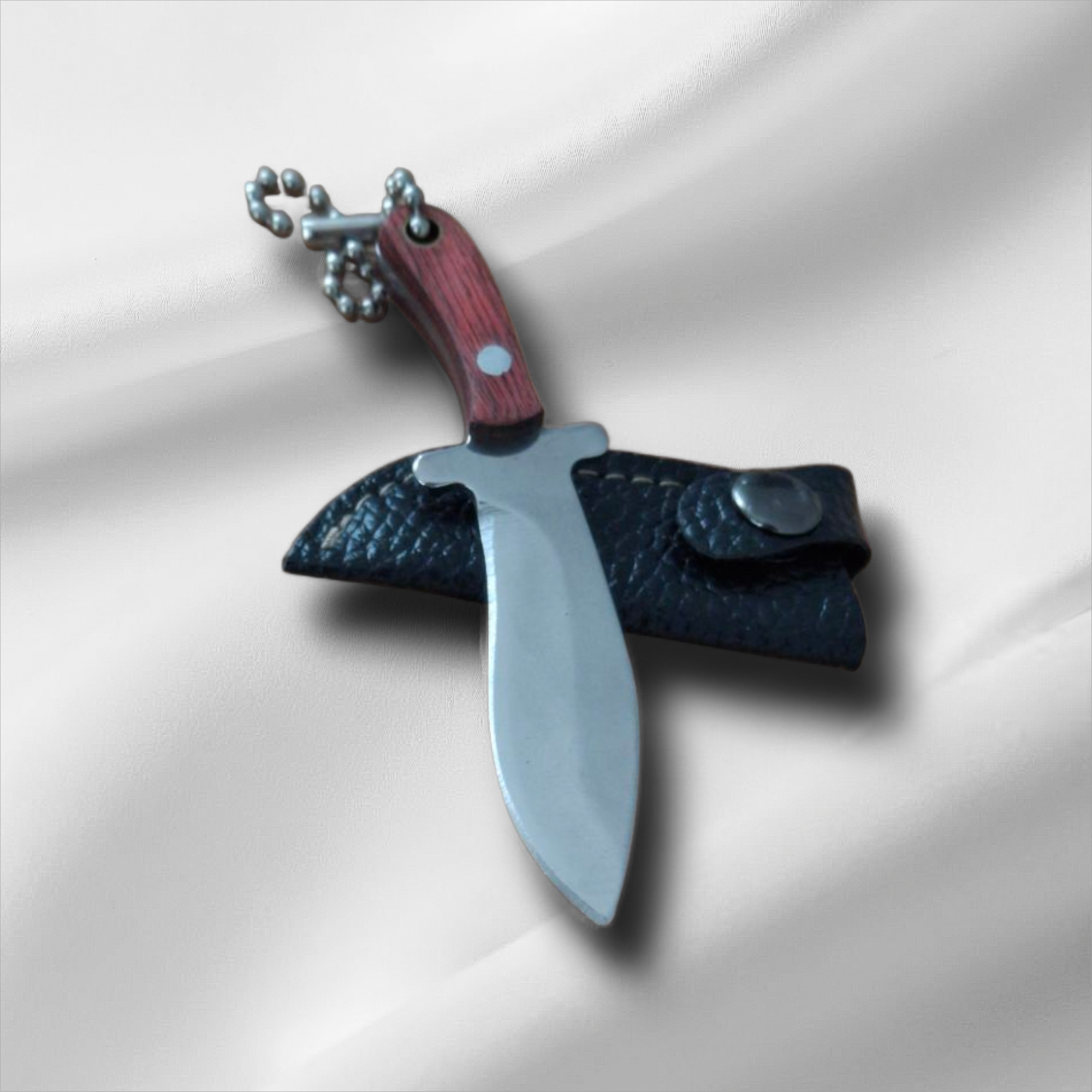 Джобен ловен нож с верижка и кожен калъф върху бял плат